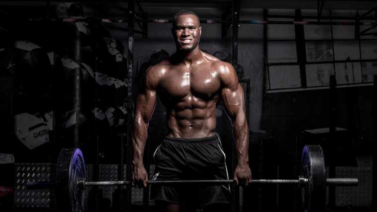 A shirtless person grimaces in exertion as they hold a loaded barbell at the top of a deadlift.