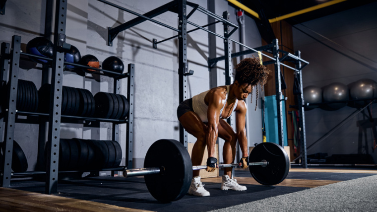 A muscular person lifting a loaded barbell off the ground with both hands in the gym
